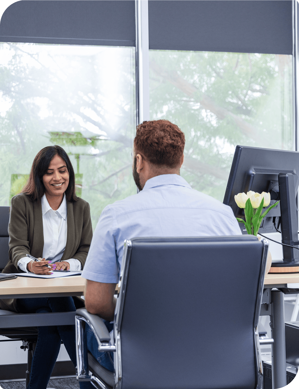 Man and woman sitting at a desk in front of a computer, with a flower vase